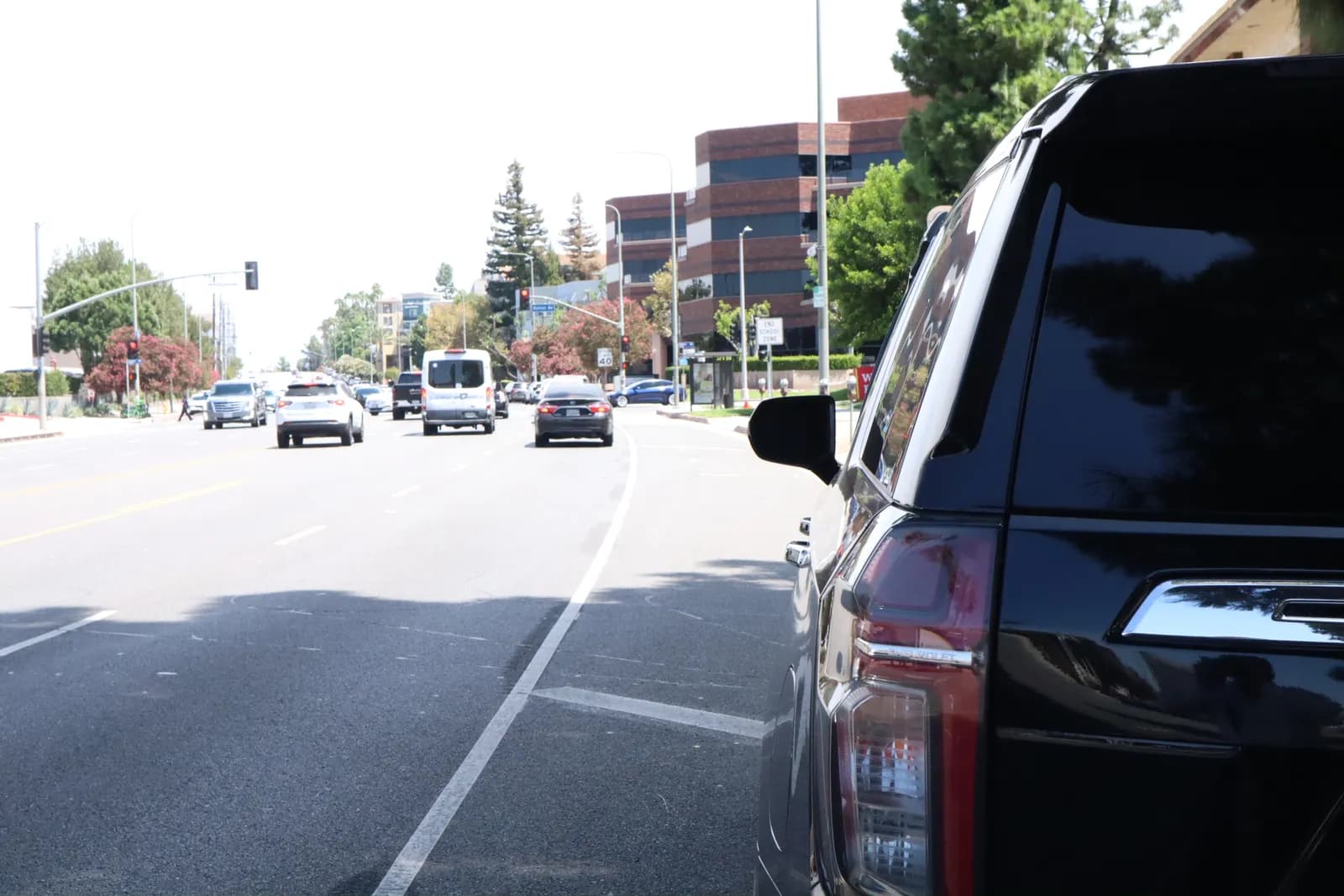 Black full-size SUV on a tree-lined city boulevard, rear three-quarter view
