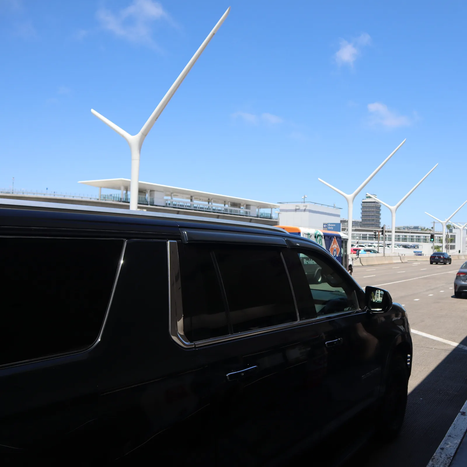 Black full-size SUV at the LAX departures curb with the airport gateway pylons and Theme Building behind