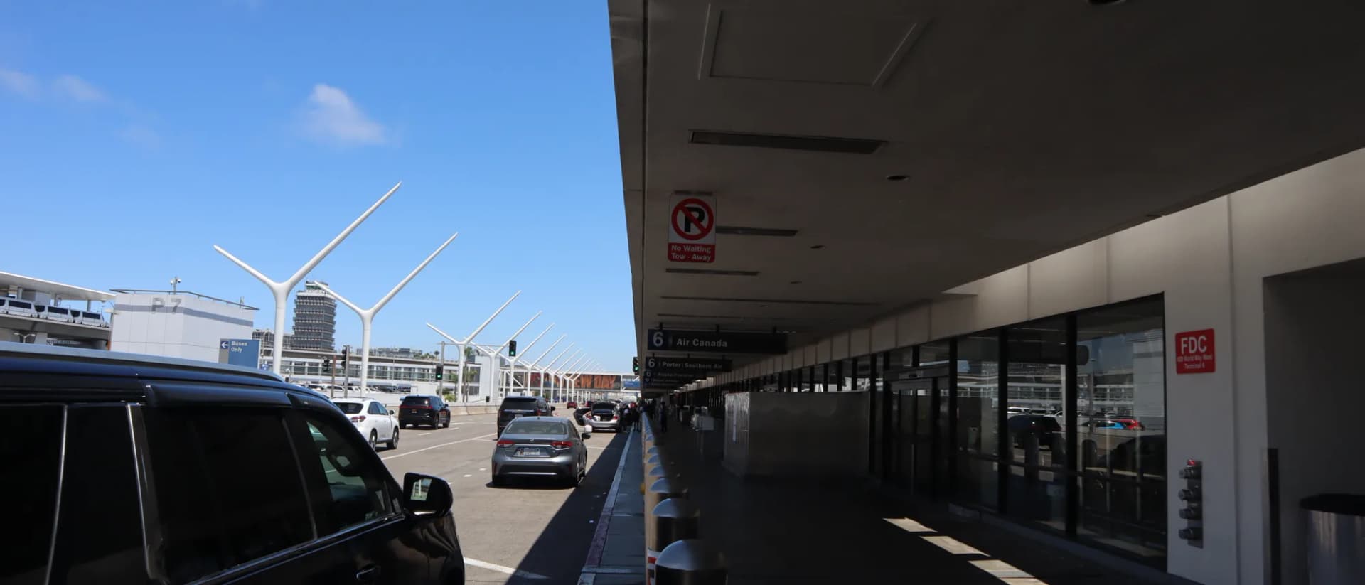 Black full-size SUV at the LAX terminal curb beside the departures walkway, with the airport pylons ahead